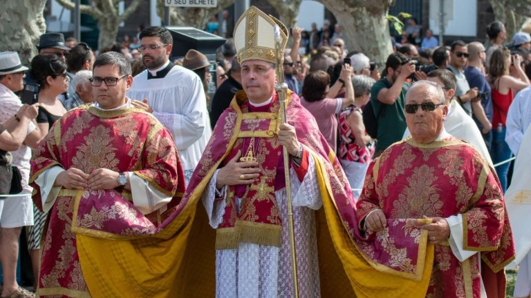 Clergy in red vestments and a crowd during an outdoor procession.