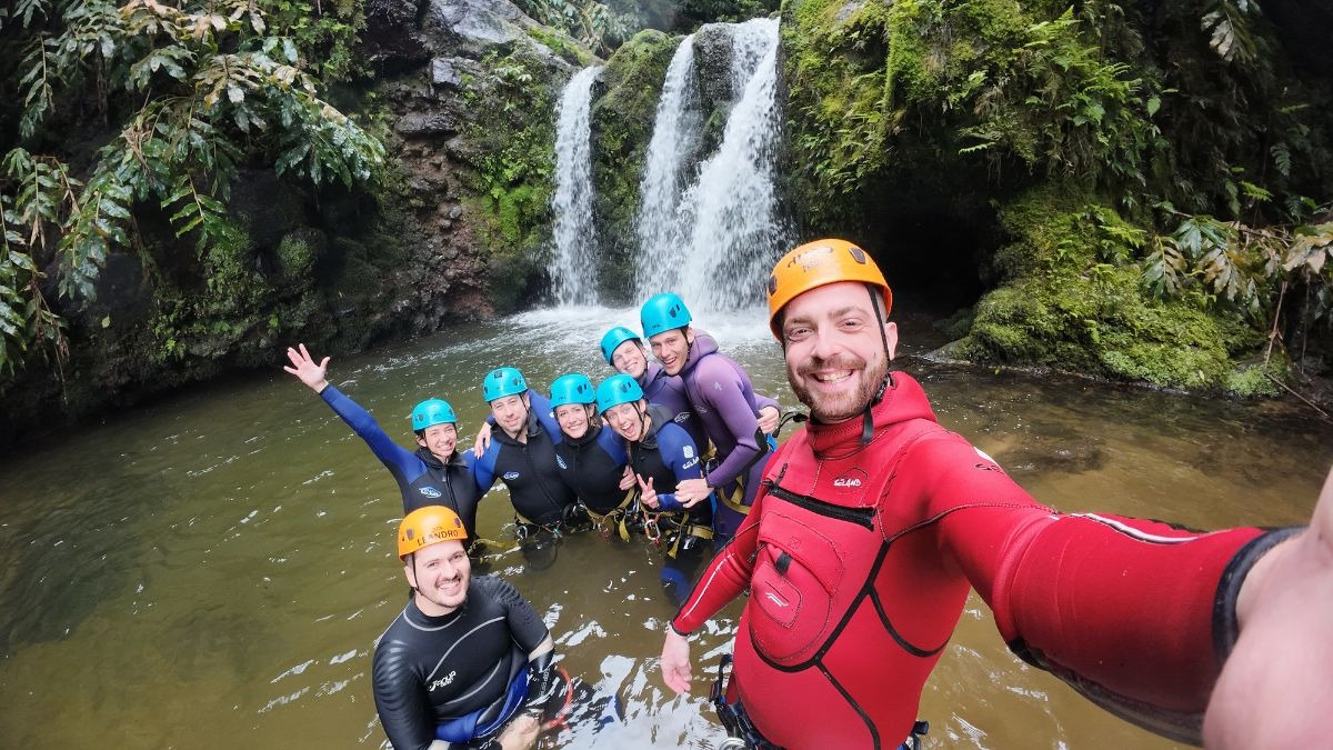 Group in wetsuits and helmets posing by a waterfall.