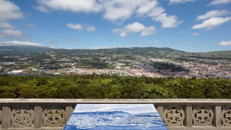Scenic view of town, hills, and clouds from a balcony with a blue-tiled map.