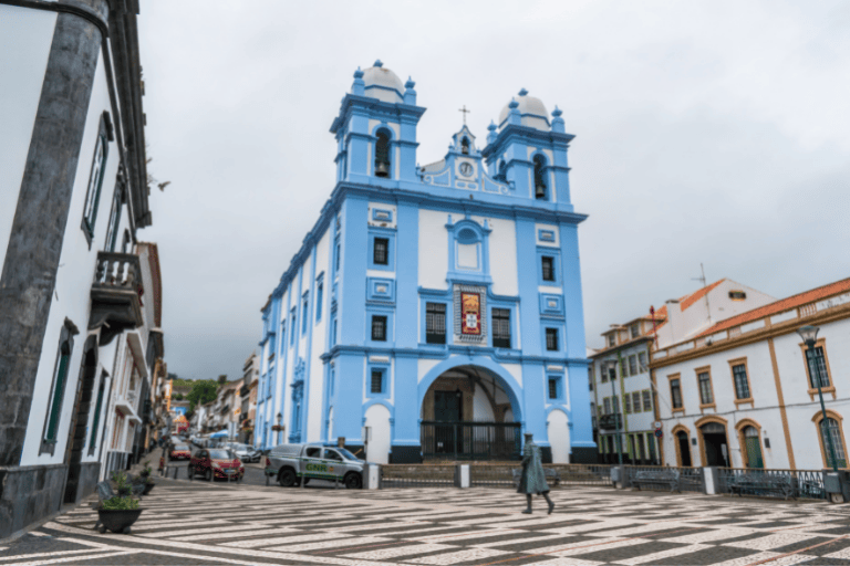 A blue and white church on a cobblestone plaza with cloudy skies.