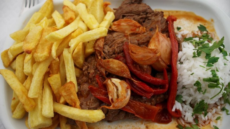 Plate with fries, grilled beef, red peppers, rice, and garnish.