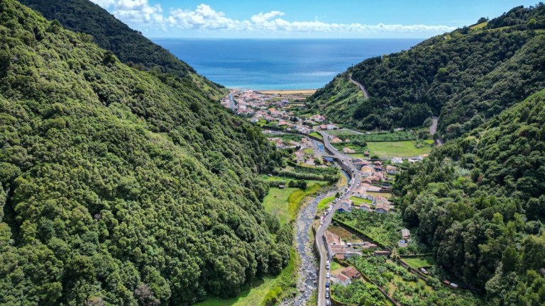 Aerial view of a valley with a river, village, and hills leading to the ocean.