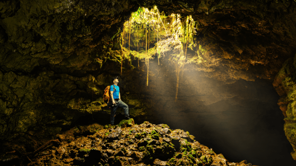 Person in a cavern, sunlight shining through a hole above.