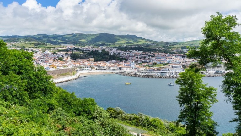 Coastal town with lush greenery, hills, and cloudy sky.