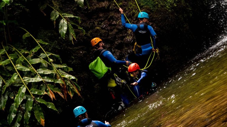 People in helmets and gear canyoning by a waterfall.
