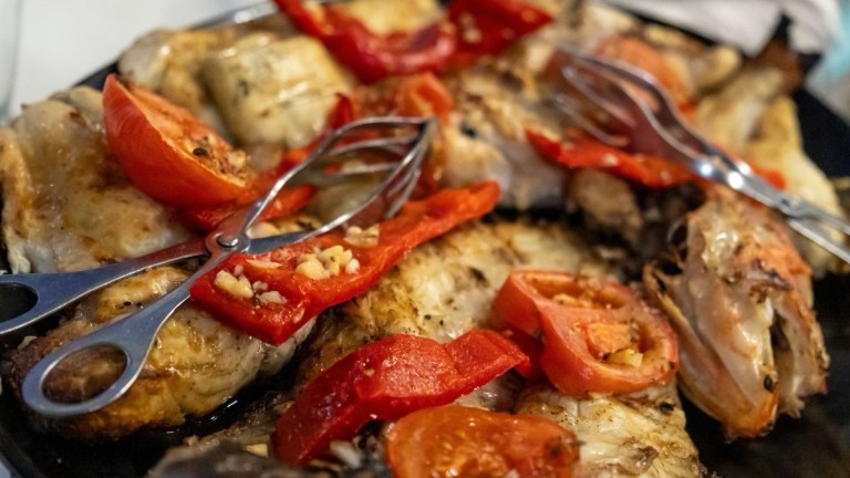 Grilled fish with tongs and sliced red peppers on top