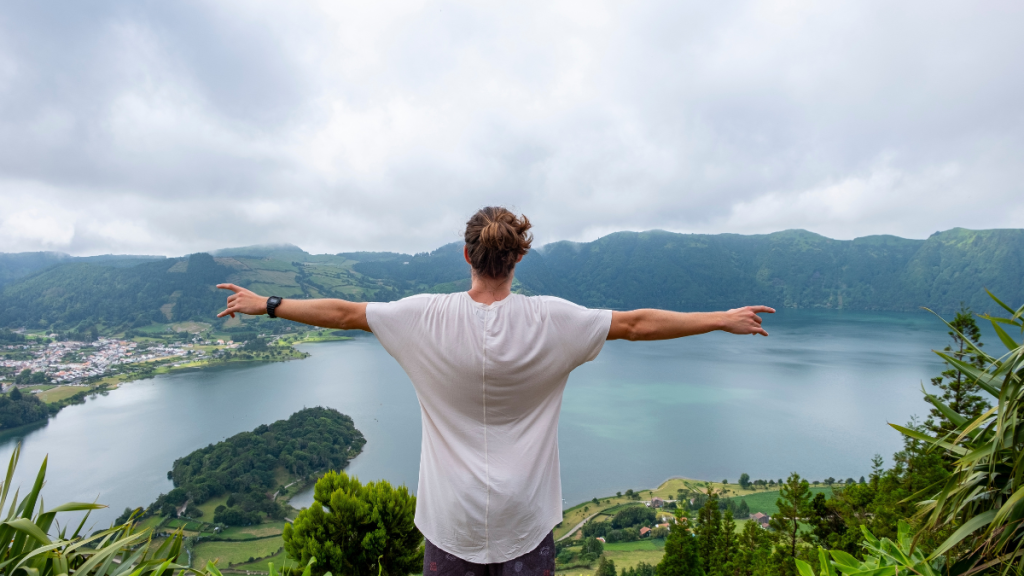 Person with arms outstretched overlooking a scenic lake and mountains.