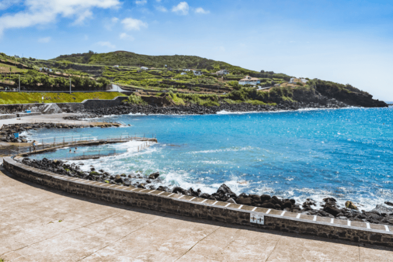 Coastal landscape with turquoise sea and terraced green hills under a blue sky.