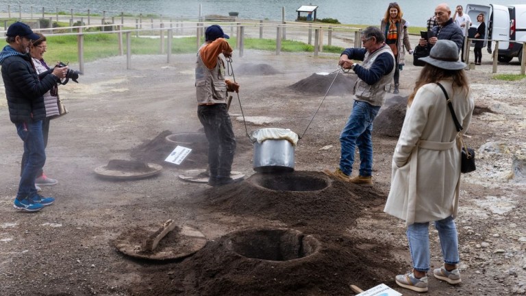 People watching a cooking demonstration with pots in steaming ground pits.