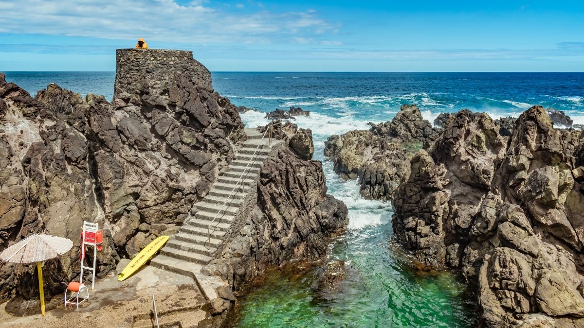 Rocky coast with stairs, umbrella, kayak, and ocean view.