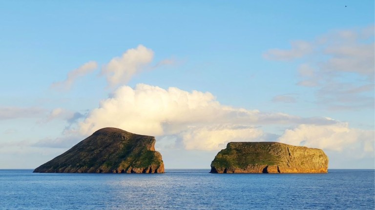 Two grassy islands in a calm sea under a partly cloudy sky.
