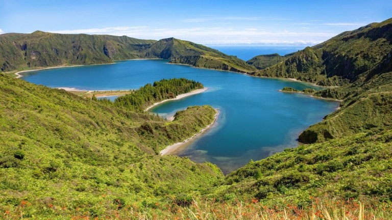 A scenic view of a large blue lake surrounded by lush green hills under a clear blue sky.