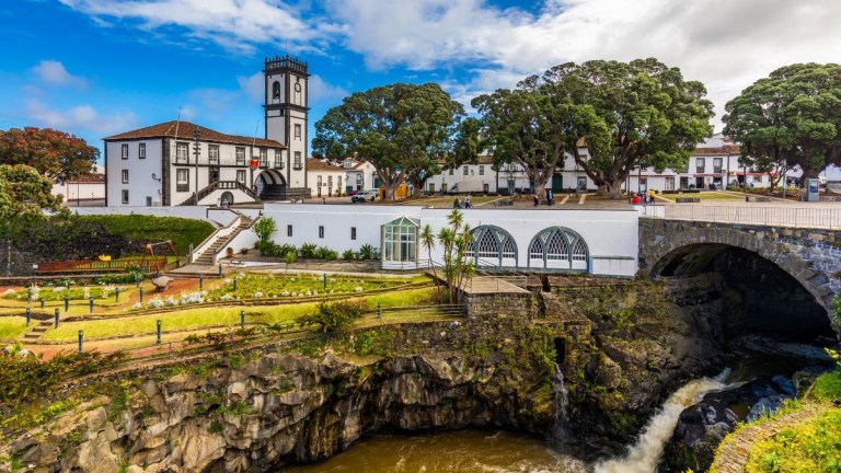 Historic church with a clock tower near lush gardens and waterfall.