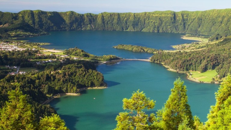 A scenic view of a lake surrounded by lush green mountains and forests.