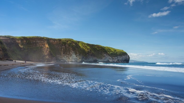 Sandy beach with cliffs and blue sky on a sunny day.