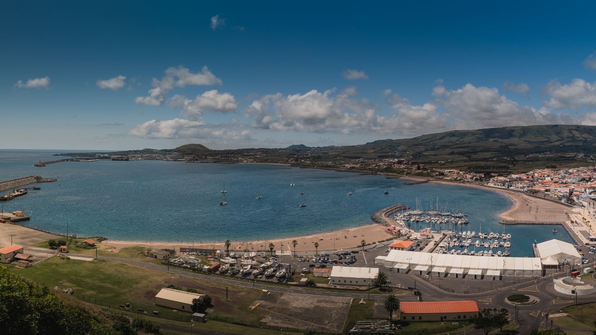Panoramic view of a coastal town with a beach and marina under a blue sky.