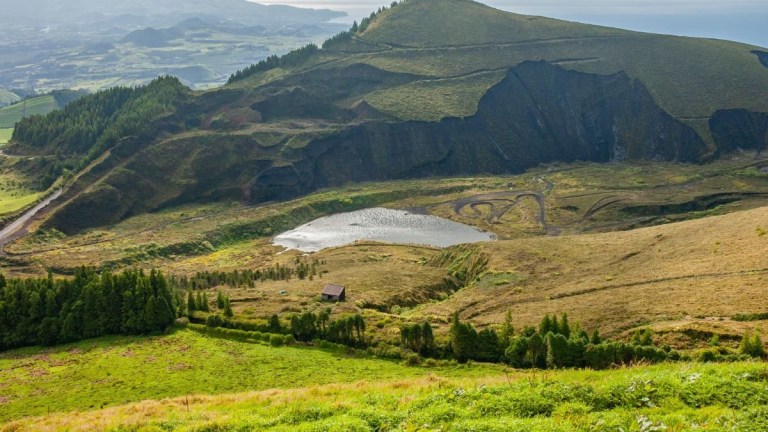 Lush green hills with a small lake and distant ocean view.