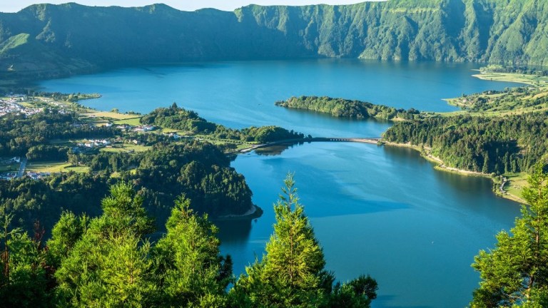 Scenic view of a lake surrounded by lush green hills under a clear blue sky.