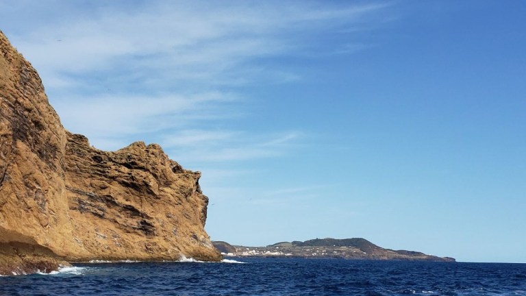 Rocky coastline under blue sky with distant buildings.