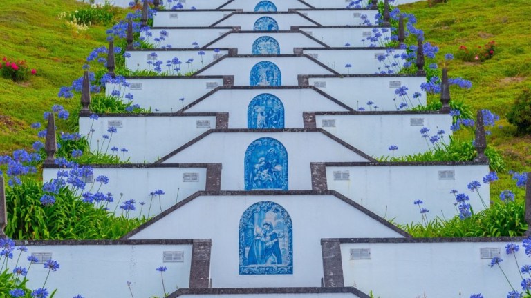 Staircase with blue tiles and flowers on a grassy hill.