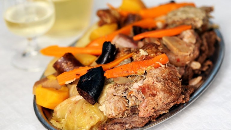 Platter of roasted meat and vegetables with a glass of white wine.