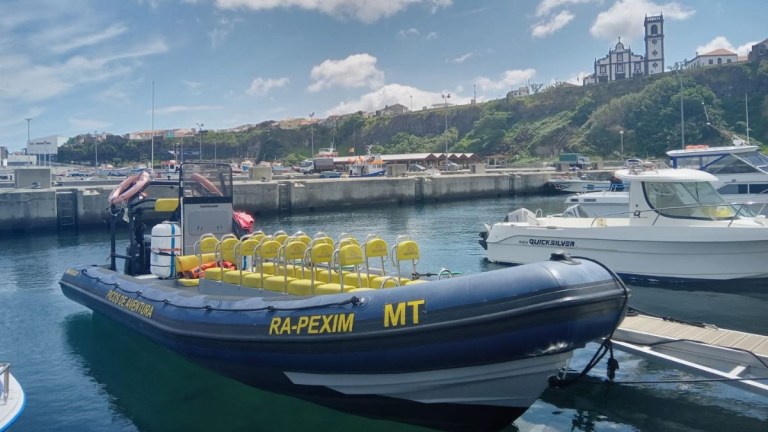 Inflatable boat docked in a marina with yellow seats, buildings and cliff in the background.