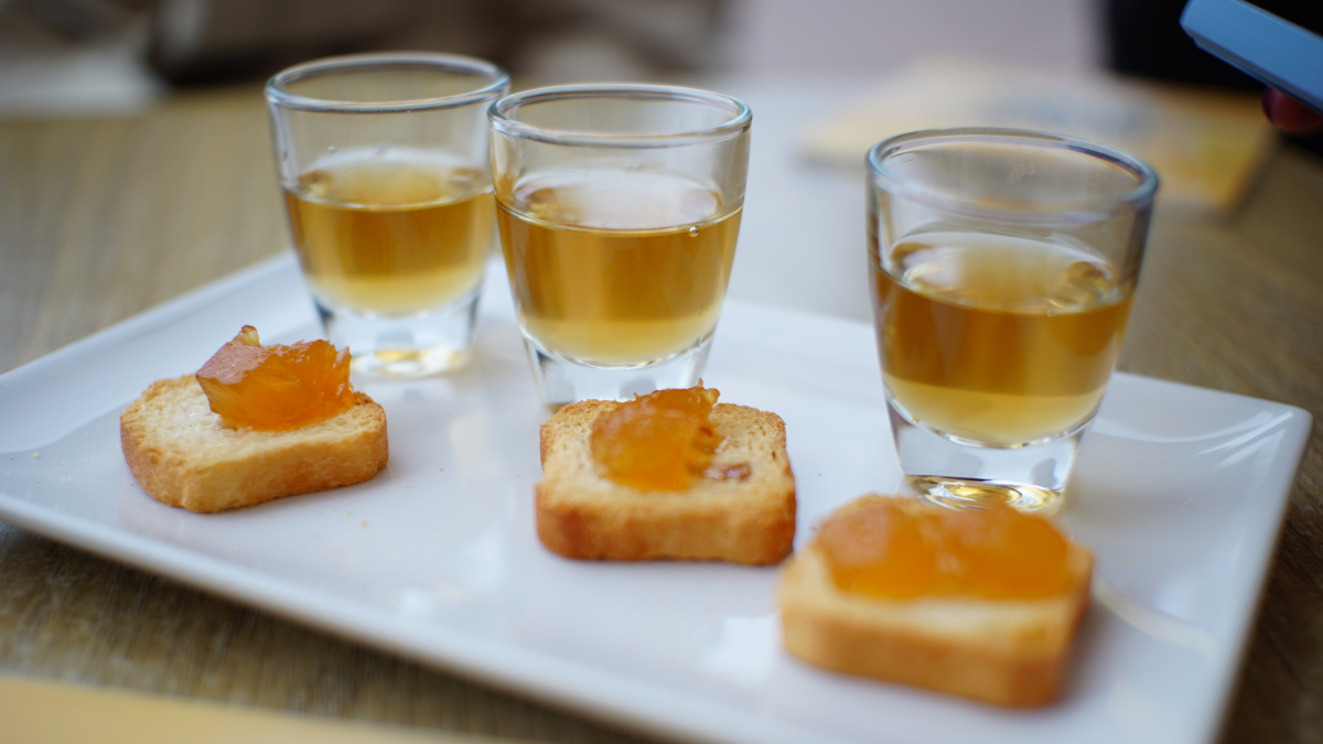 Three glasses of amber liquid and toast with jam on a white plate.
