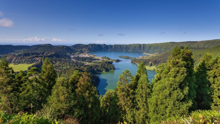 Panoramic view of two lakes surrounded by lush green forest and mountains under a clear blue sky.