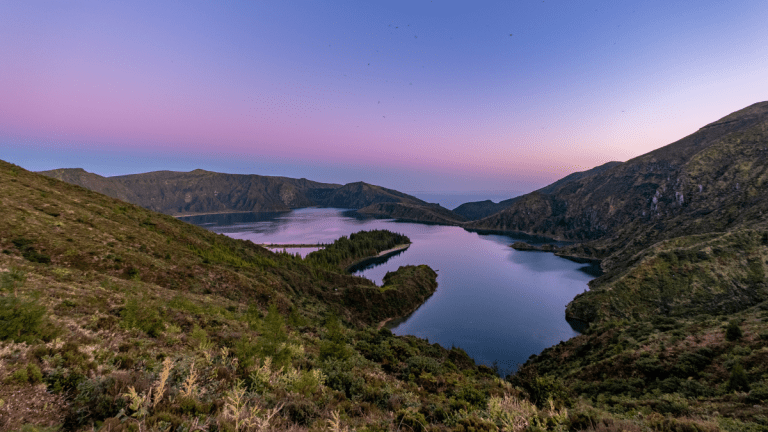 Lake surrounded by rolling hills at sunset, with a clear sky.