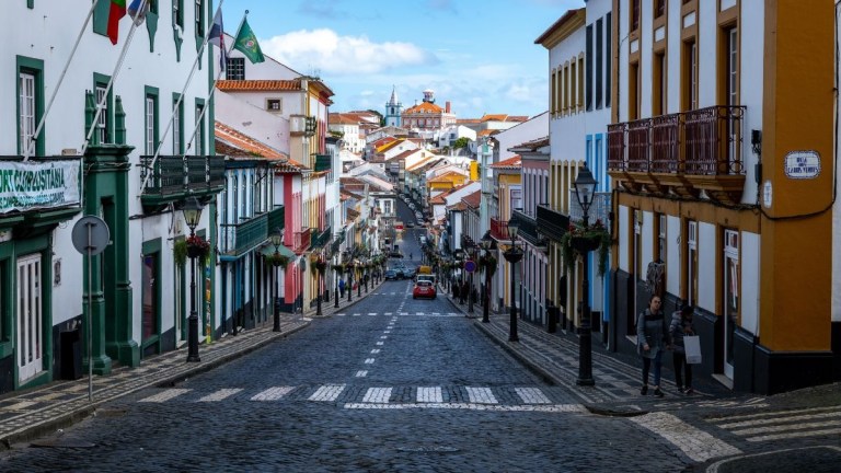 Narrow cobblestone street with colorful buildings leading to town at the horizon.