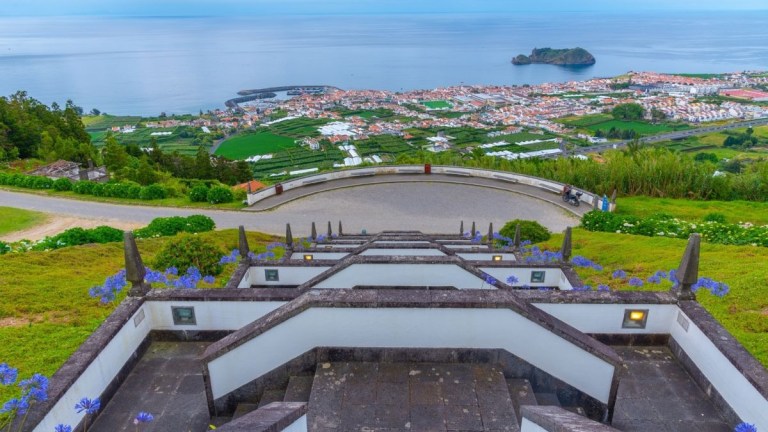 Scenic view from hilltop steps overlooking town, ocean, and small island.