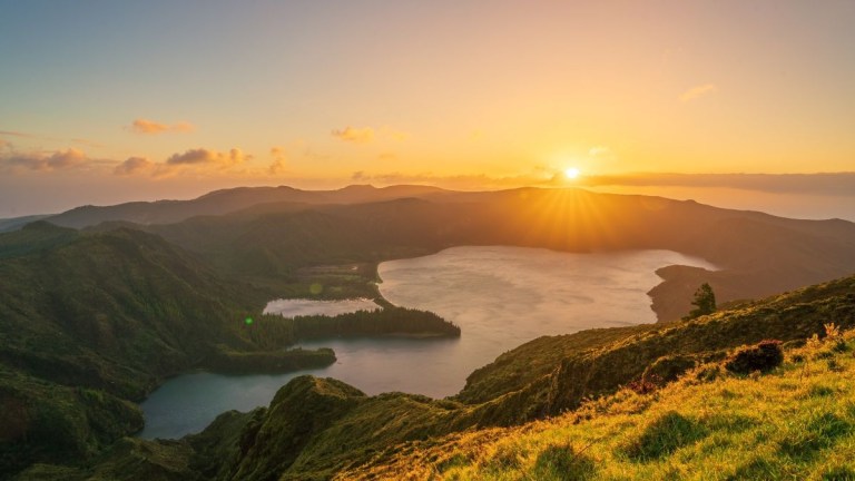 Sunset over hilly landscape with lakes and a clear sky.