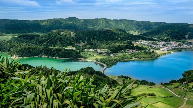 A view of two lakes in a green valley, one blue and one green, with a small village nearby.