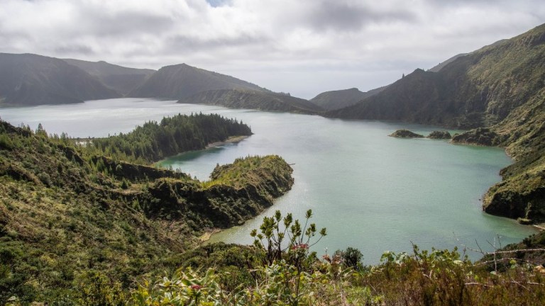Scenic view of a lake surrounded by mountains under a cloudy sky.
