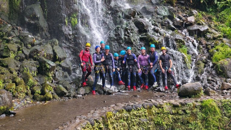 Group of people in helmets standing by a waterfall.