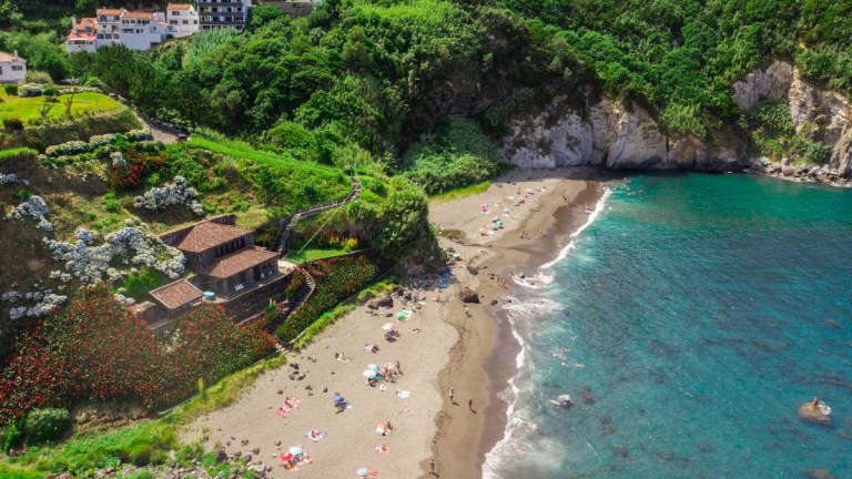 Aerial view of a beach with people, surrounded by lush greenery and cliffs.