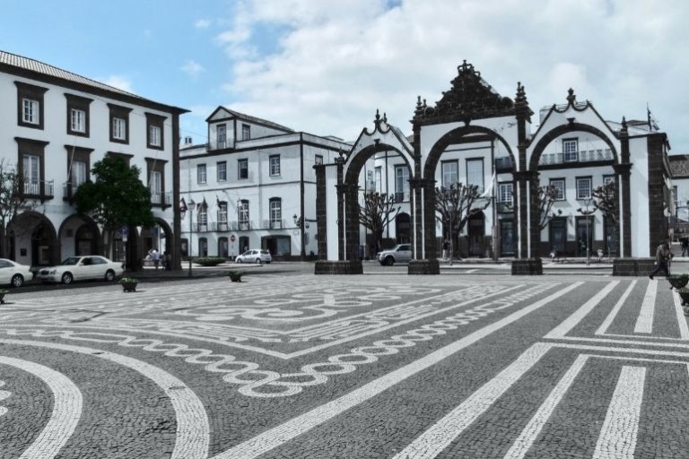 Town square with patterned stone pavement and archways, surrounded by classic buildings.