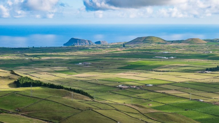 Aerial view of patchwork farmland leading to the ocean under a cloudy sky.