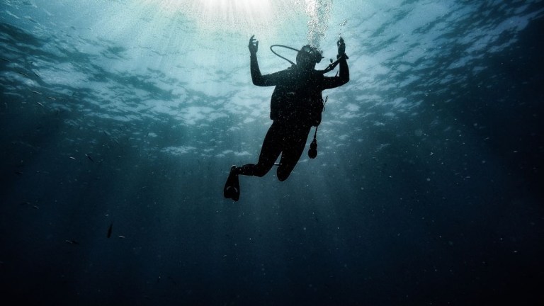Silhouette of a scuba diver underwater with light rays filtering through the water.