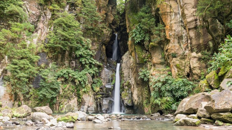 Tall waterfall cascading down rocky cliffs surrounded by lush greenery.