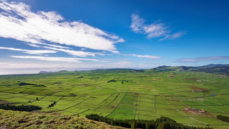 Vast green landscape with fields, hills, and a blue sky with scattered clouds.