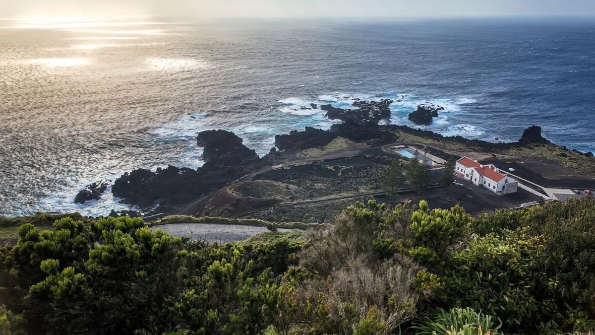 Coastal landscape with rocky shore, greenery, and a white house near the ocean.