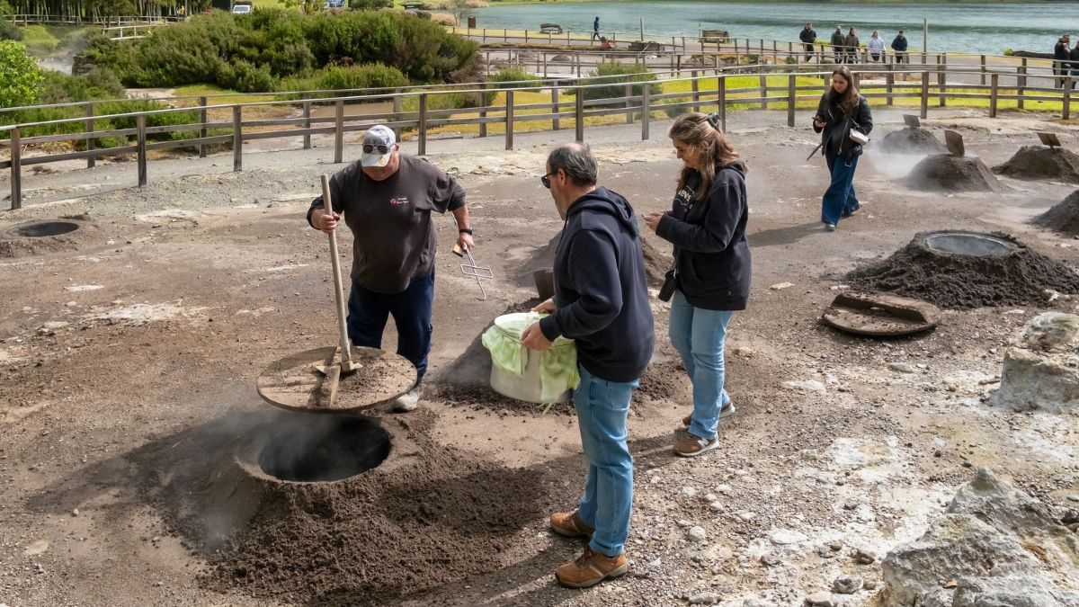 People cooking in geothermal steam vents near a lake with a wooden fence.