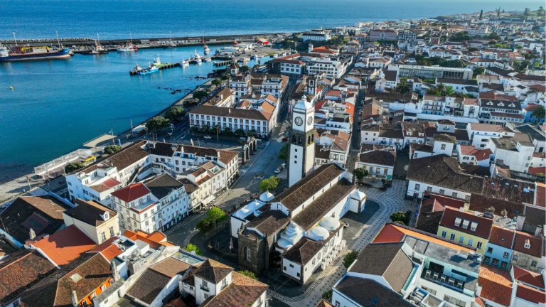 Aerial view of a coastal town with a clock tower and colorful buildings near a harbor.