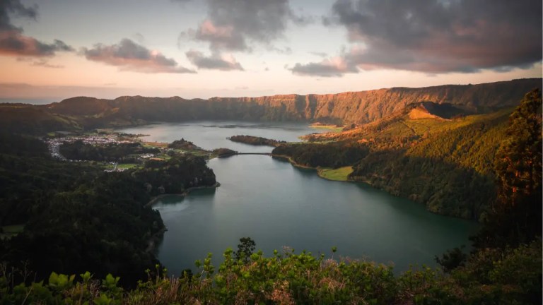 Scenic lake surrounded by mountains at sunset with clouds overhead.