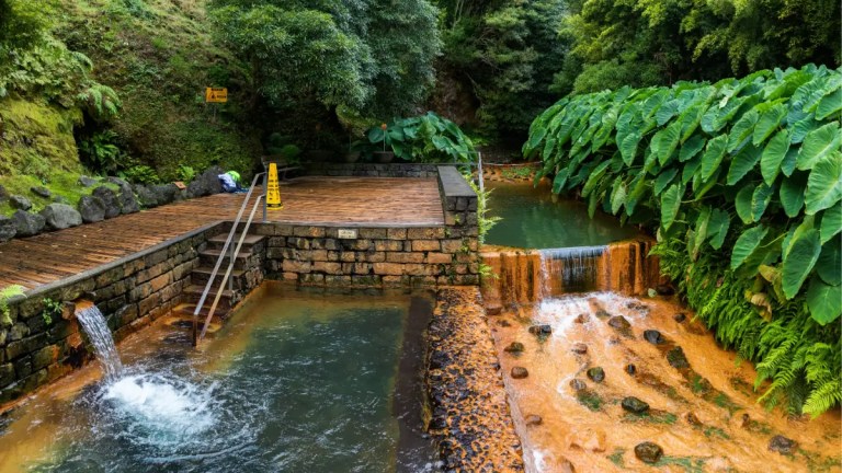 Natural hot spring with wooden deck, flowing water, and lush greenery.