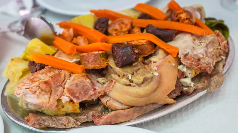 A platter of assorted cooked meats and vegetables with carrots on top.